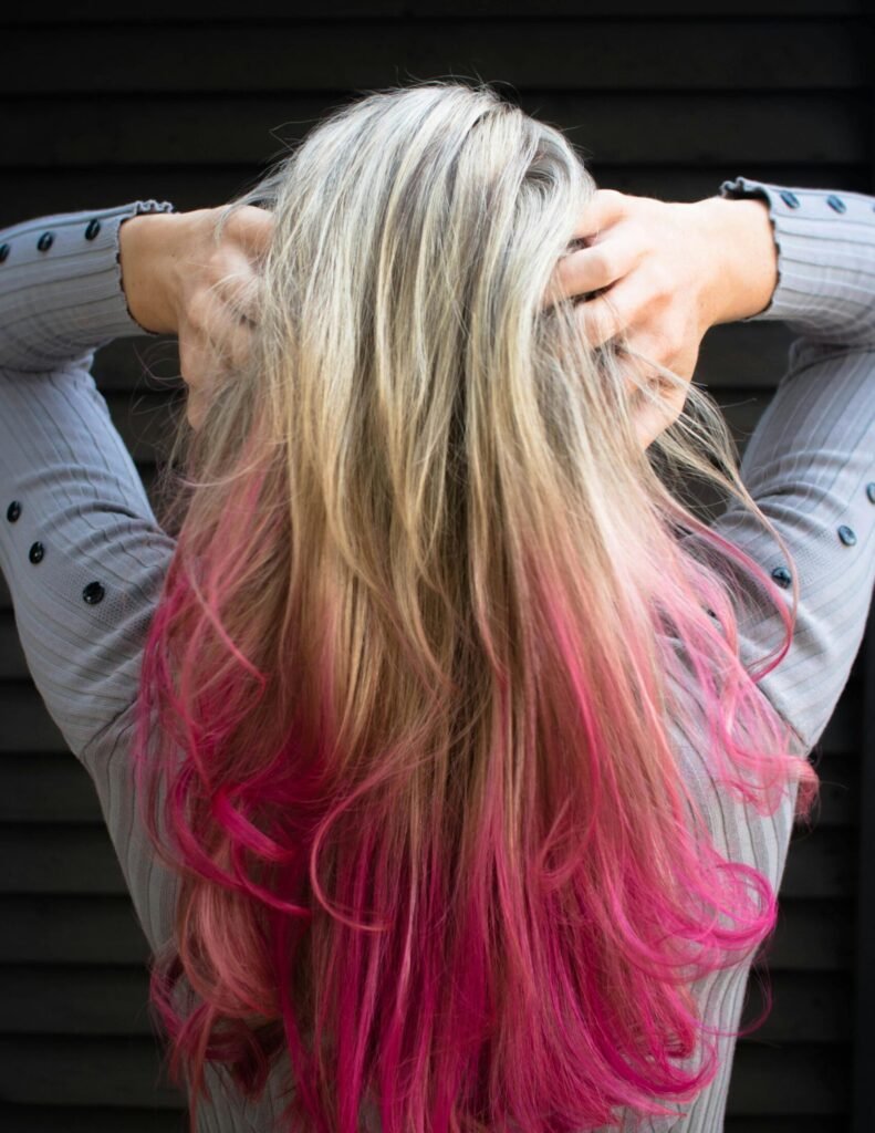 Close-up of a woman with blonde and pink ombre hair in a stylish pose.