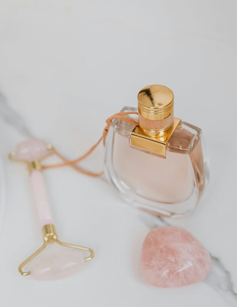 Close-up of a luxury perfume bottle with a jade roller and rose quartz on elegant marble.